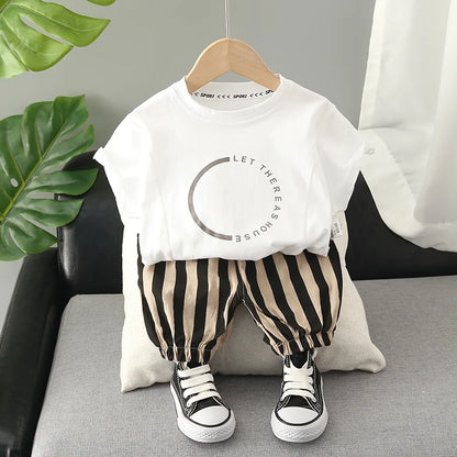 Baby outfit with white graphic t-shirt, striped pants, and black sneakers on sofa