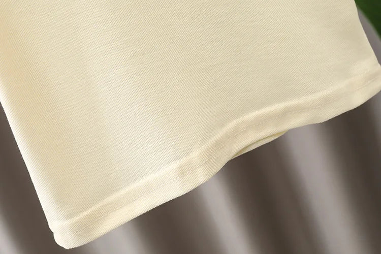 Detail of cream cotton baby clothing fabric with stitched hem, soft texture close-up