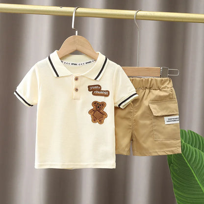 Infant summer set with cream polo shirt featuring teddy bear patch and khaki shorts, hanging on rack