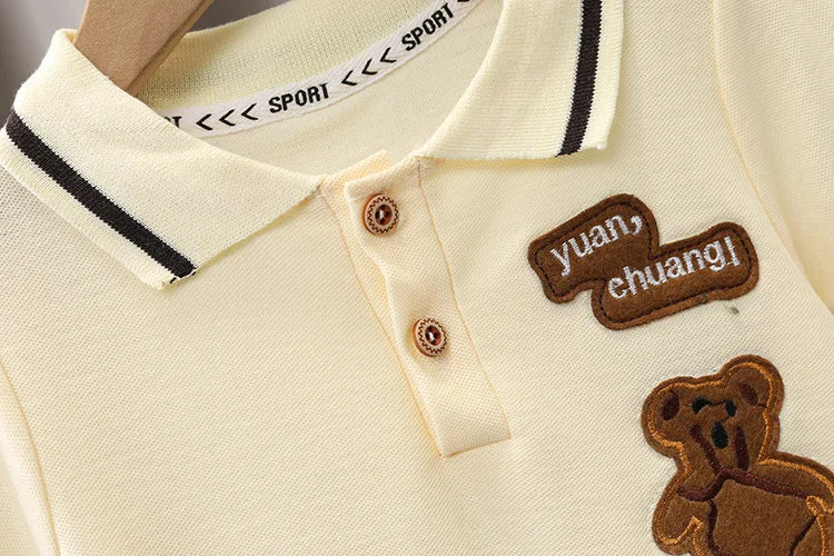 Beige baby polo shirt with teddy bear patch, button collar and embroidered text details