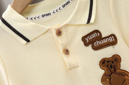 Beige baby polo shirt with teddy bear patch, button collar and embroidered text details